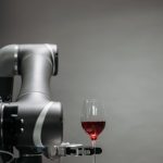 A robotic arm delicately handles a glass of red wine against a gray background.
