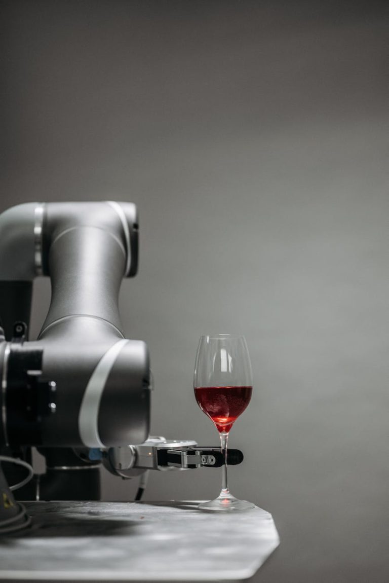A robotic arm delicately handles a glass of red wine against a gray background.