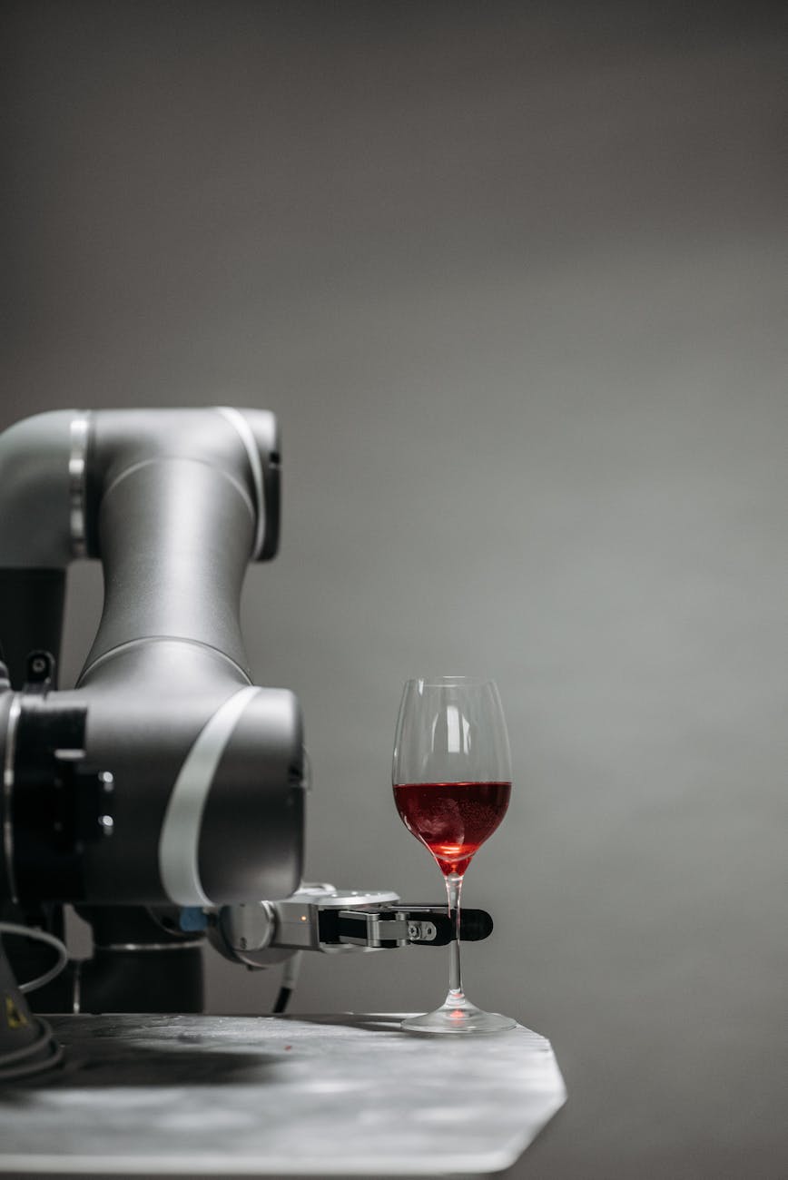 A robotic arm delicately handles a glass of red wine against a gray background.