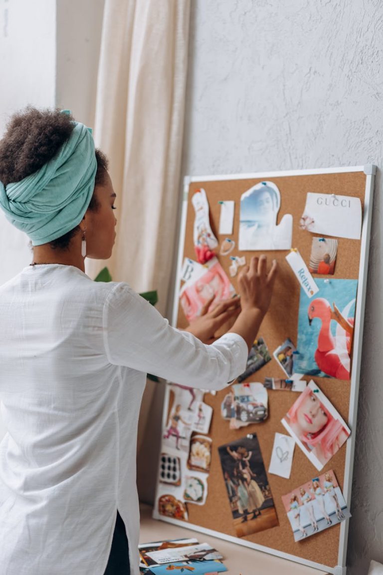 Side view of a woman in headscarf arranging photos on a cork board, embracing creativity.