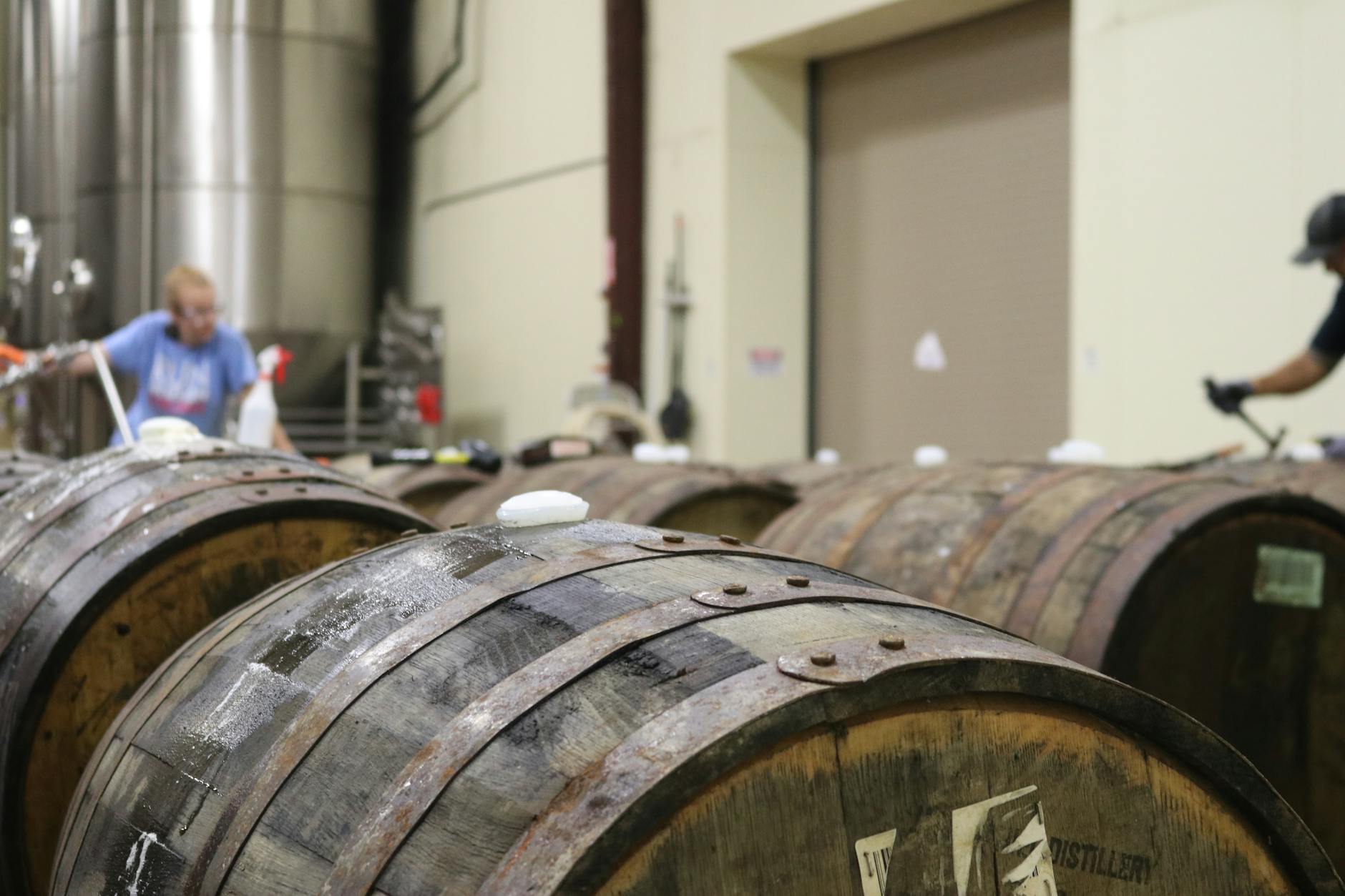 A distillery interior featuring wooden barrels. Workers are busy in the background, showcasing the production process.