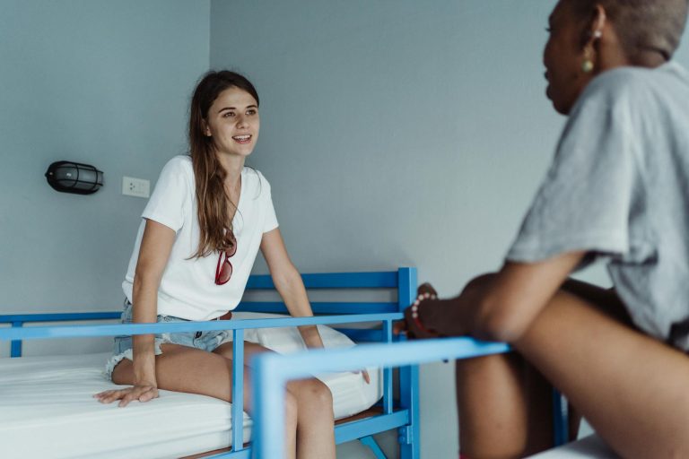 Two women engaged in a friendly conversation in a hostel room with bunk beds.