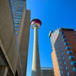 A towering view of Calgary Tower surrounded by modern skyscrapers under a clear blue sky.