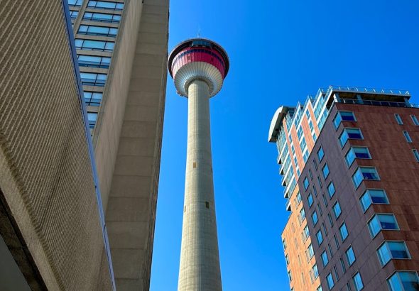 A towering view of Calgary Tower surrounded by modern skyscrapers under a clear blue sky.