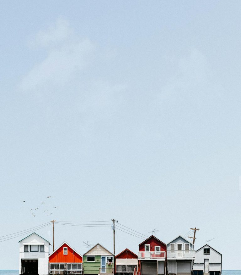 Vibrant coastal beach houses lined up against a clear blue sky, showcasing serene seaside charm.