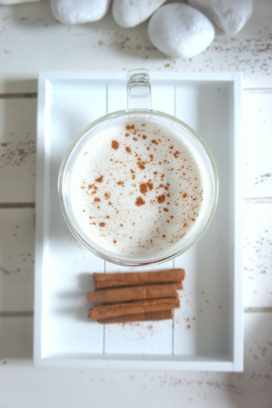 A creamy cinnamon topped drink in a clear glass mug on a wooden tray, inviting and delicious.