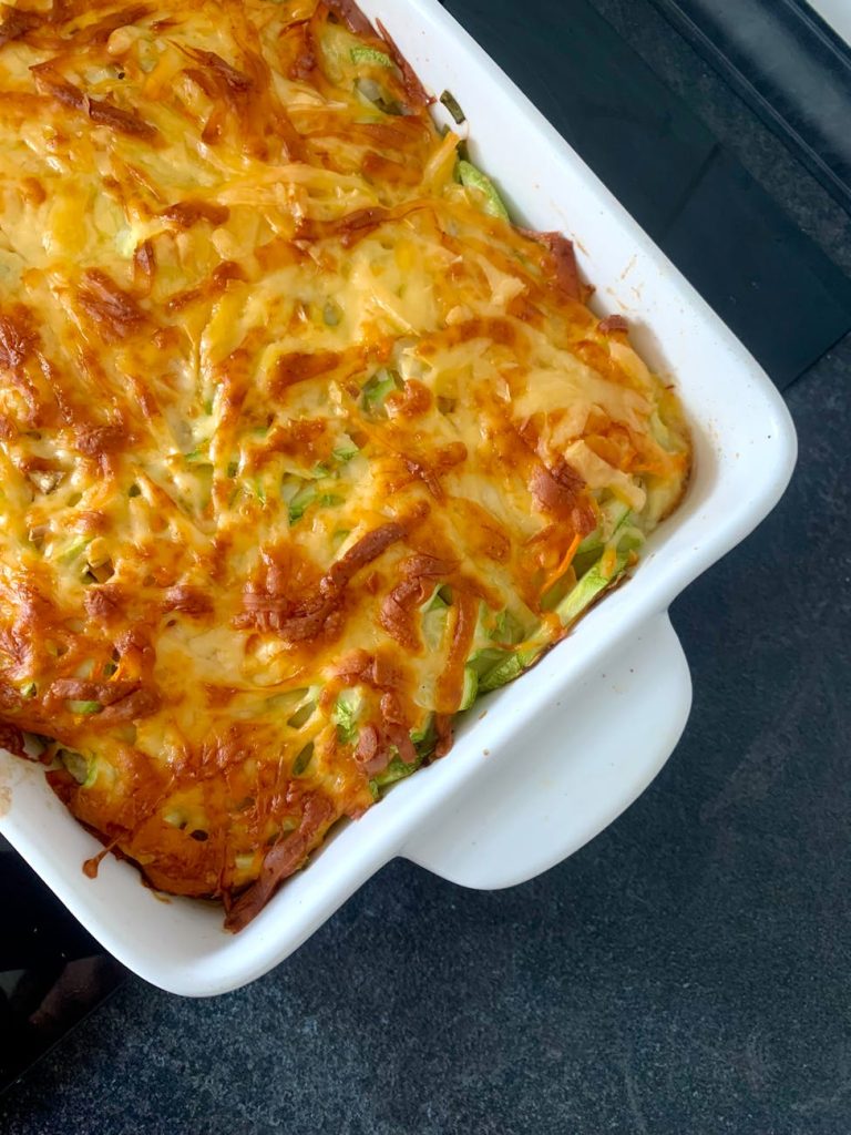 Delicious homemade cheesy baked casserole with vegetables in a white dish on dark countertop.