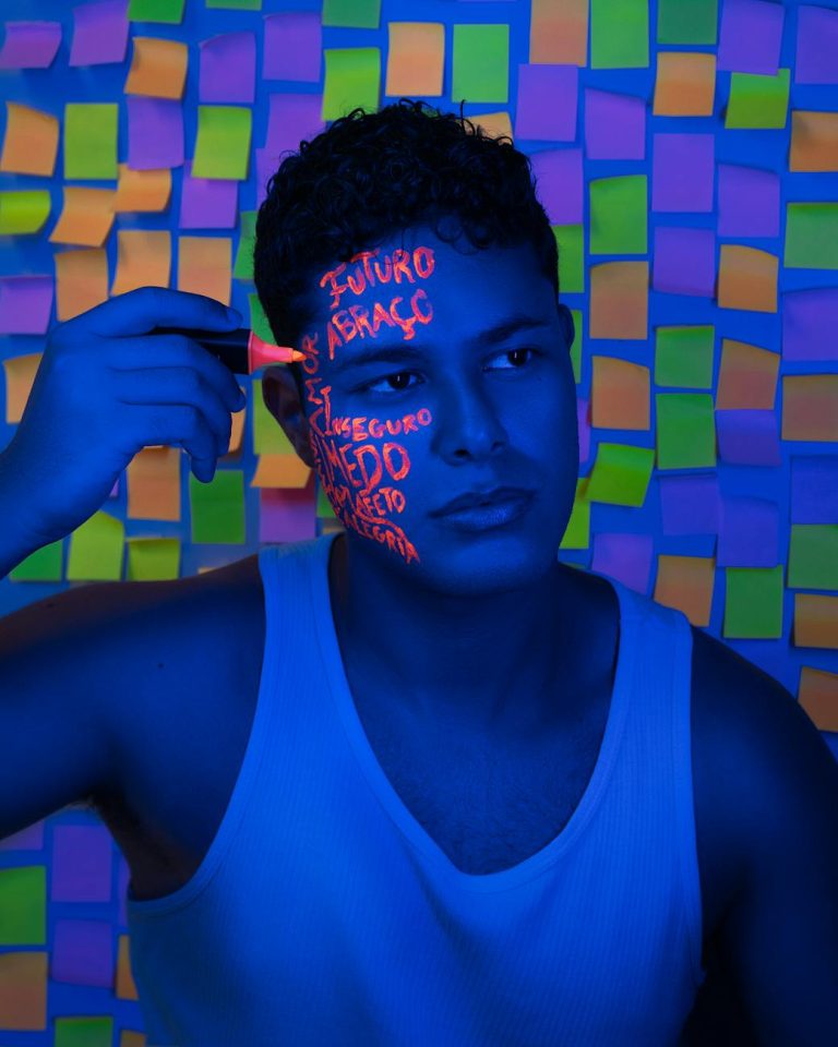 Man with neon face paint and sticky notes background in blue lighting.