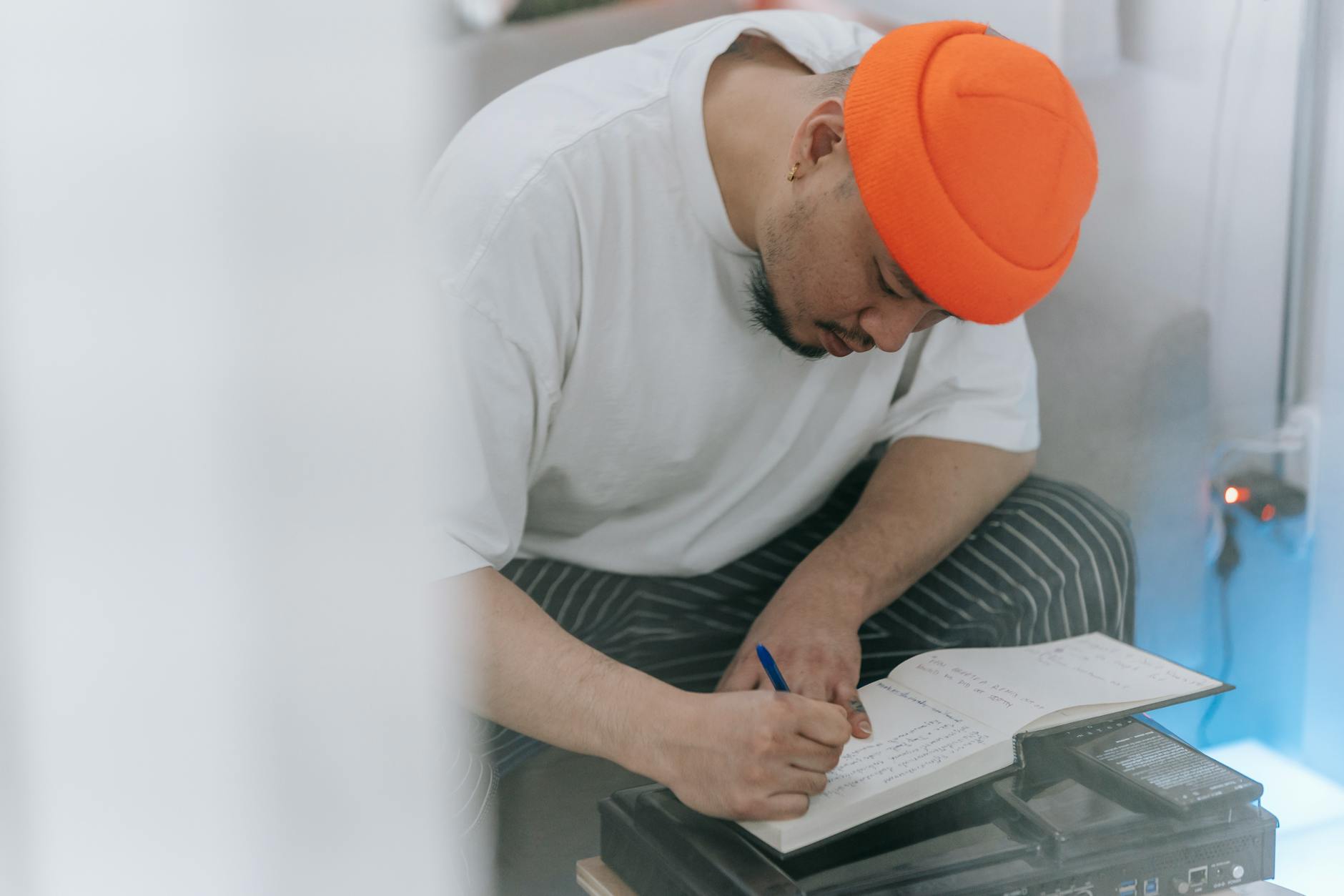 Man in an orange beanie writing in a notebook, showcasing creativity and focus.