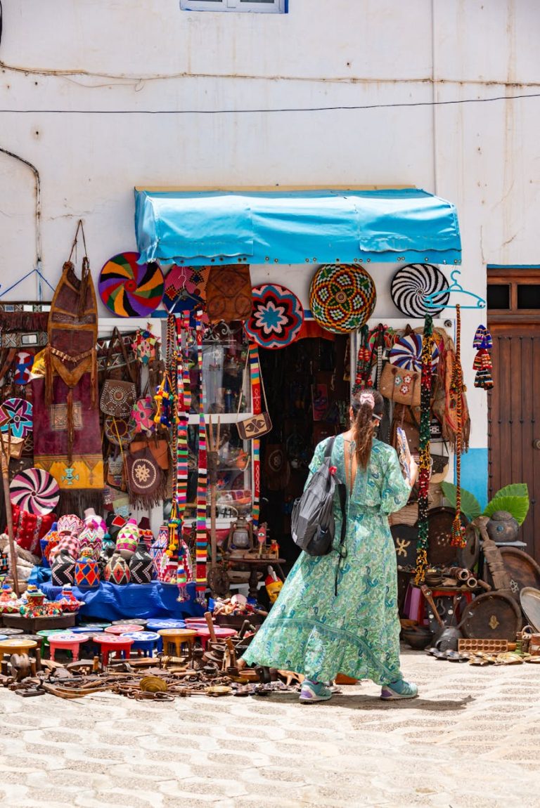 A woman in a dress examines vibrant handmade crafts at an outdoor market.