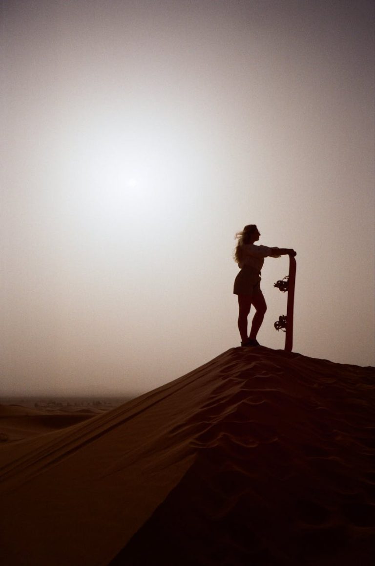 A captivating silhouette of a woman holding a sandboard on a desert dune at sunset, perfect for adventure themes.