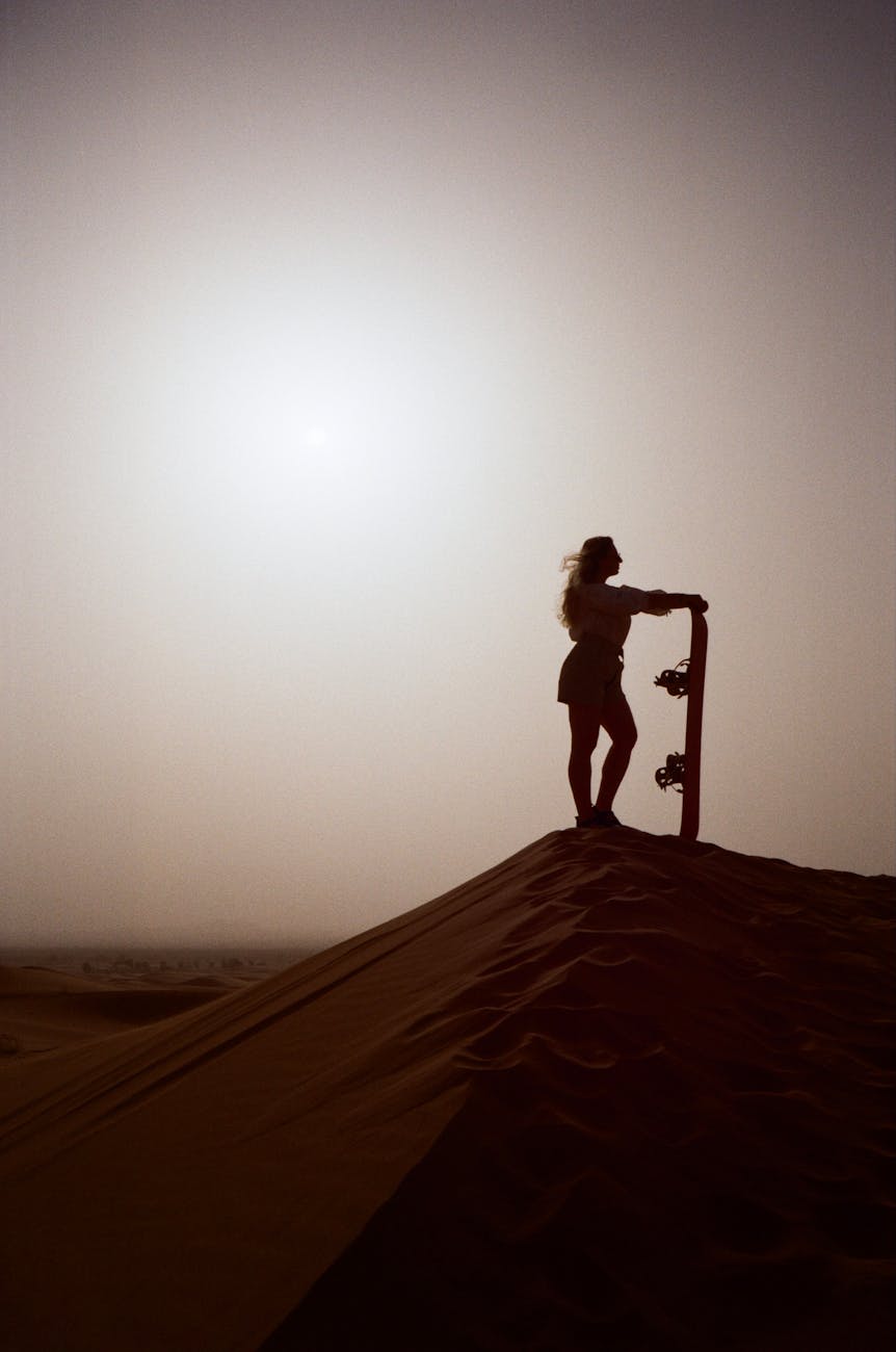 A captivating silhouette of a woman holding a sandboard on a desert dune at sunset, perfect for adventure themes.