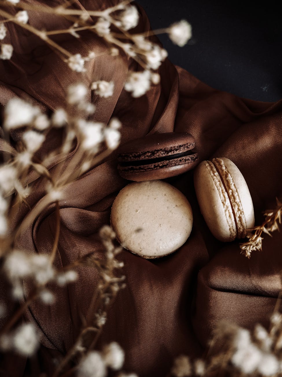Three French macarons elegantly displayed on brown fabric, surrounded by delicate flowers.