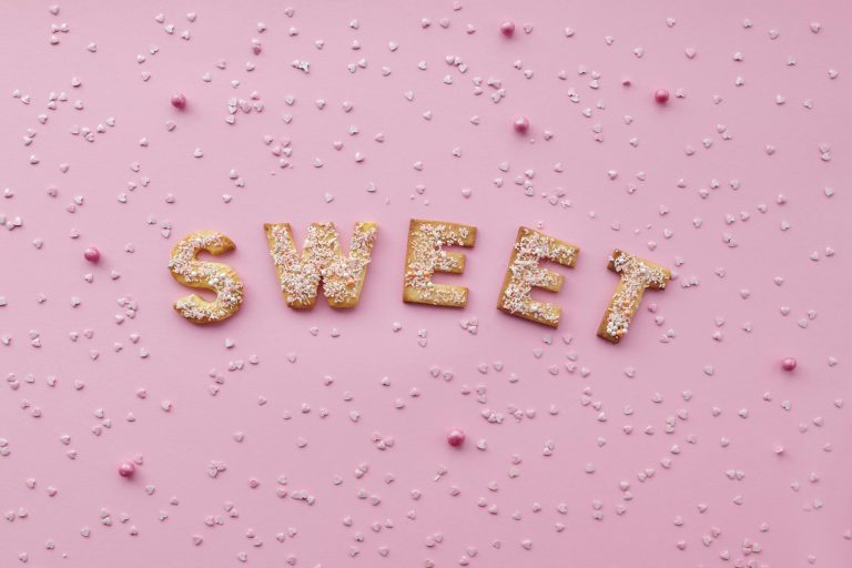 Flat lay of sweet letter cookies on a pink background with sprinkles.