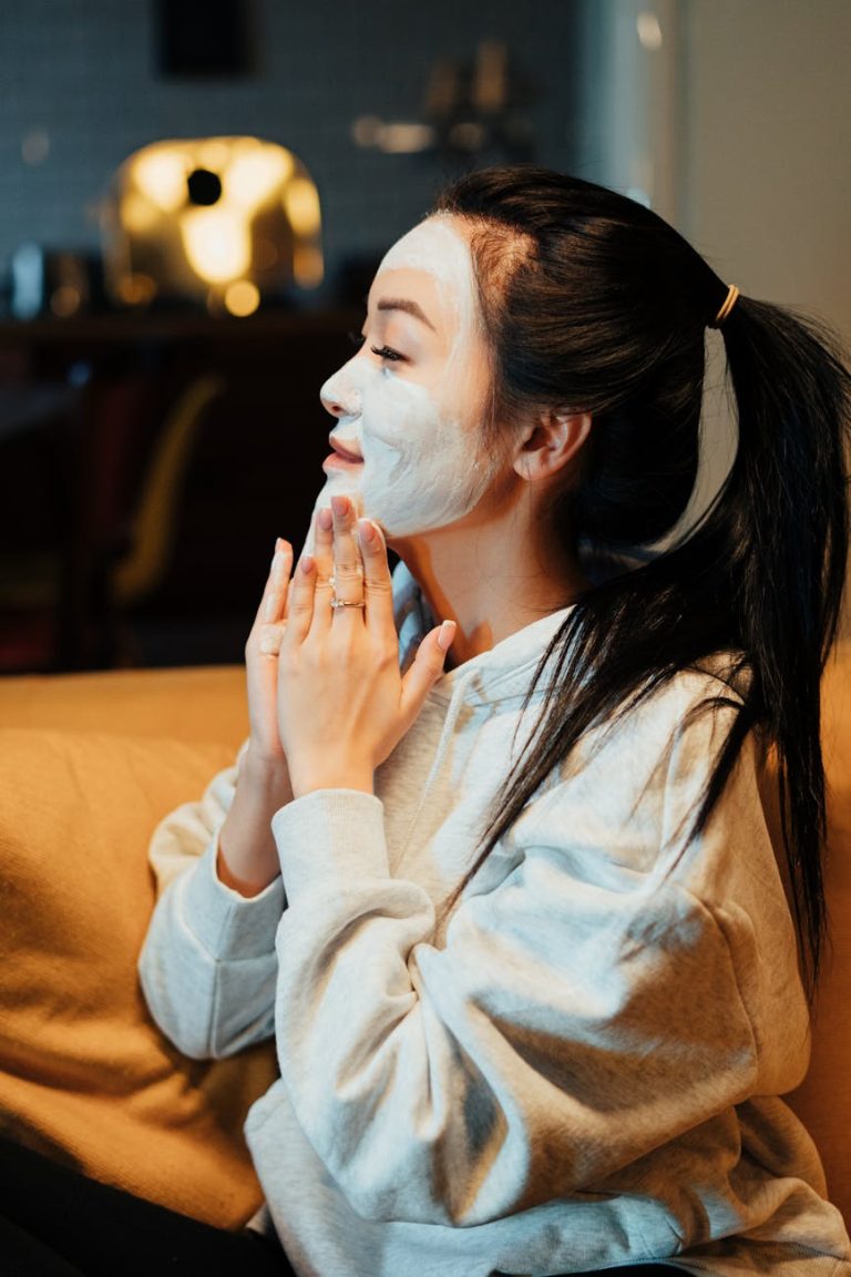 Asian woman relaxing with a face mask, practicing skincare in a cozy home environment.