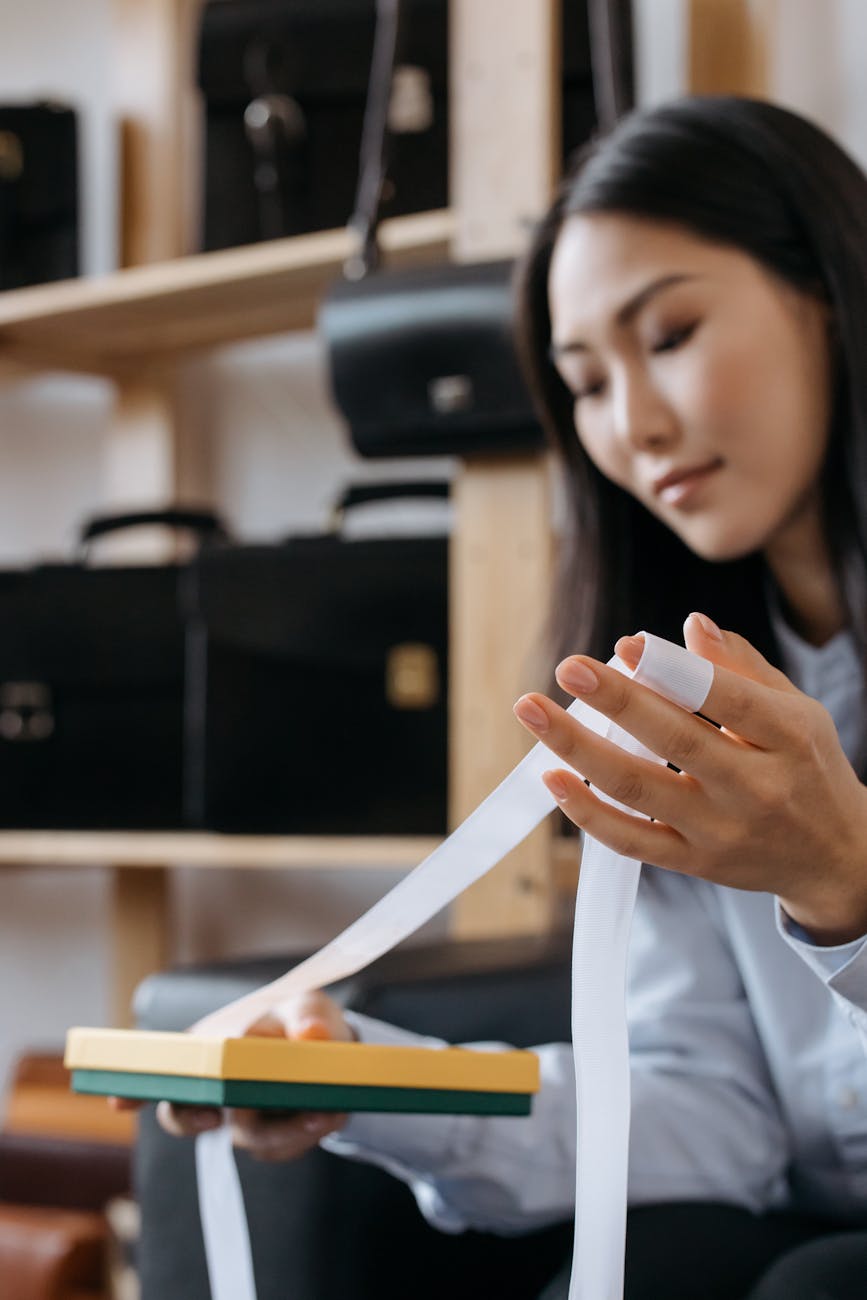 A young Asian woman wrapping a gift box with ribbon in a store setting.
