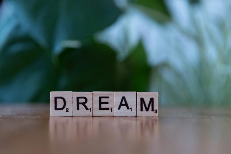 Wooden blocks spell 'Dream' on a table with a blurred green background.
