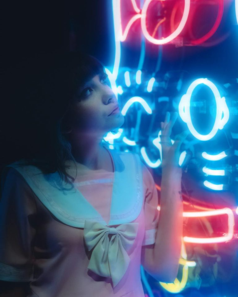 A whimsical portrait of a woman daydreaming near colorful neon lights.