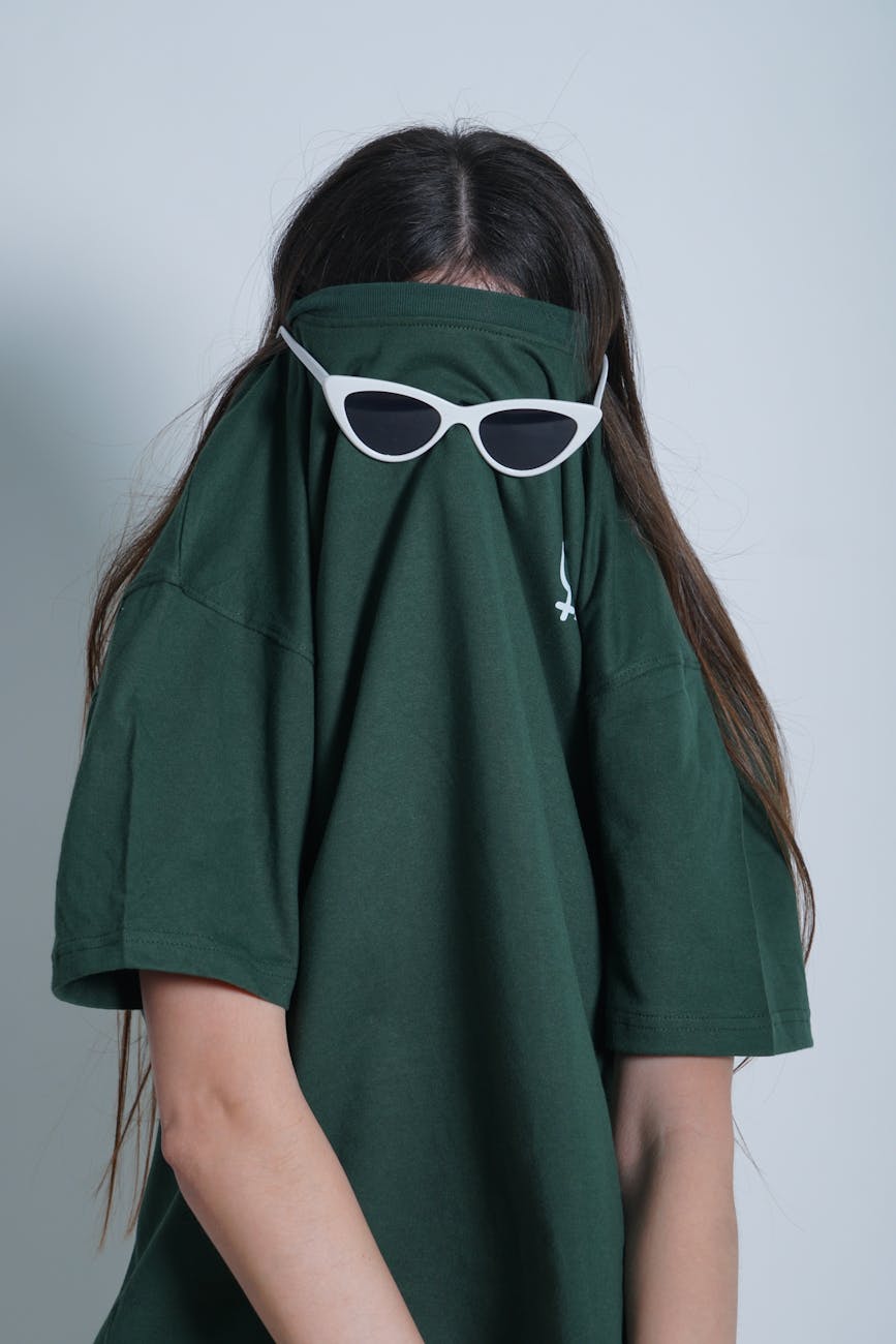 A young woman humorously poses with sunglasses over her t-shirt pulled over her head.