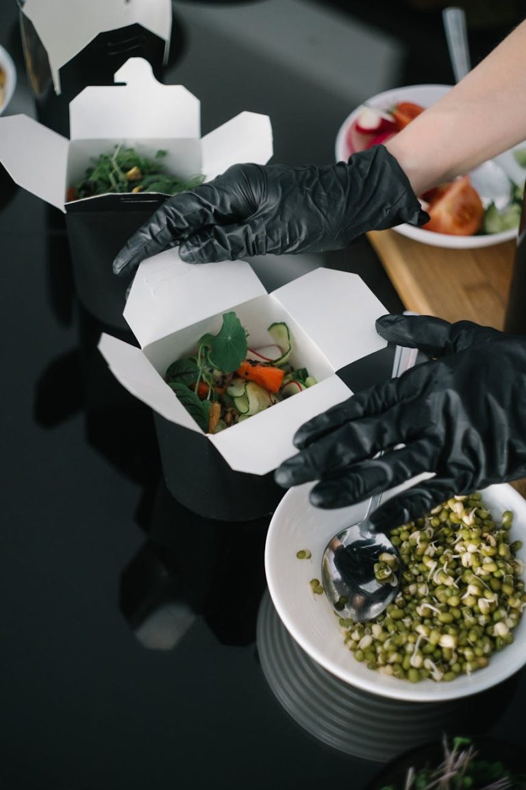 Gloved hands preparing fresh salad takeout in eco-friendly containers for delivery.