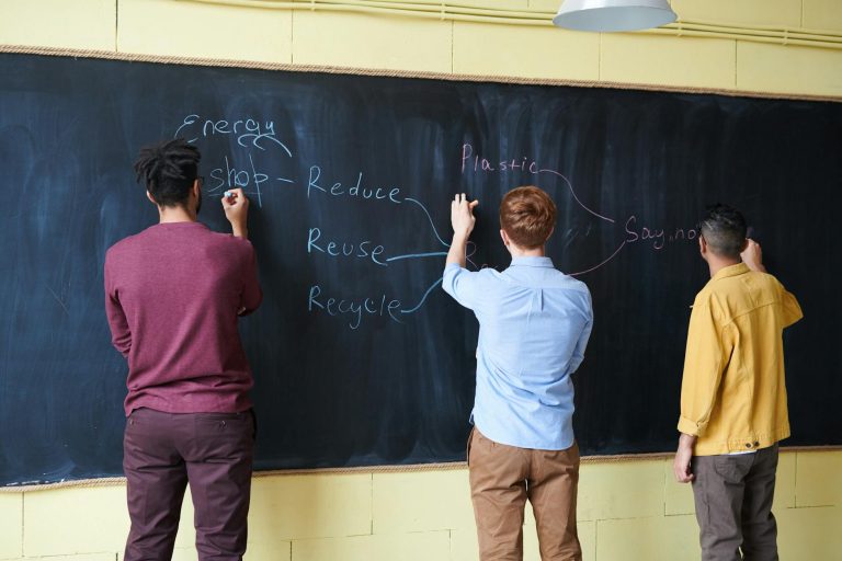 Three students writing on a chalkboard, focusing on reducing plastic and energy waste.