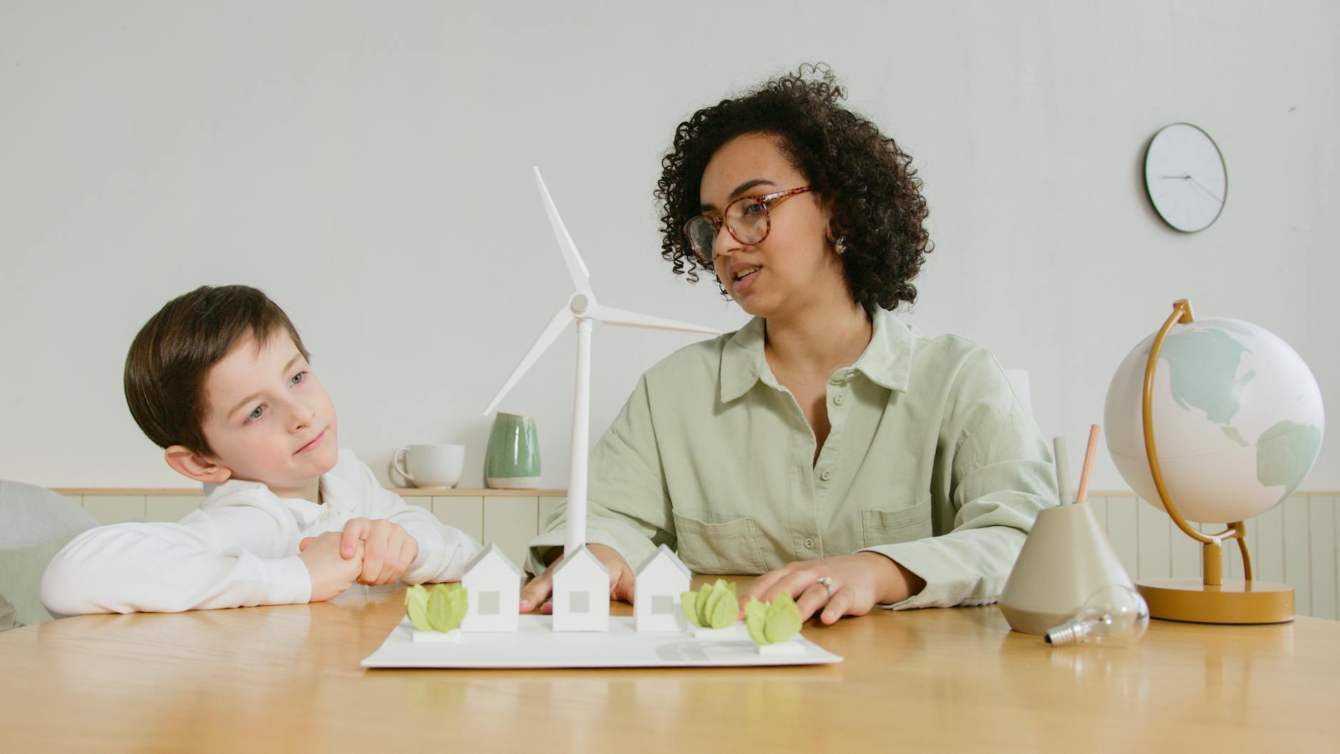 A child and teacher explore renewable energy concepts with a wind turbine model indoors.