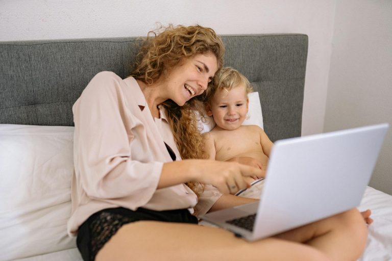 A mother and child enjoying digital time together on a bed, sharing smiles.