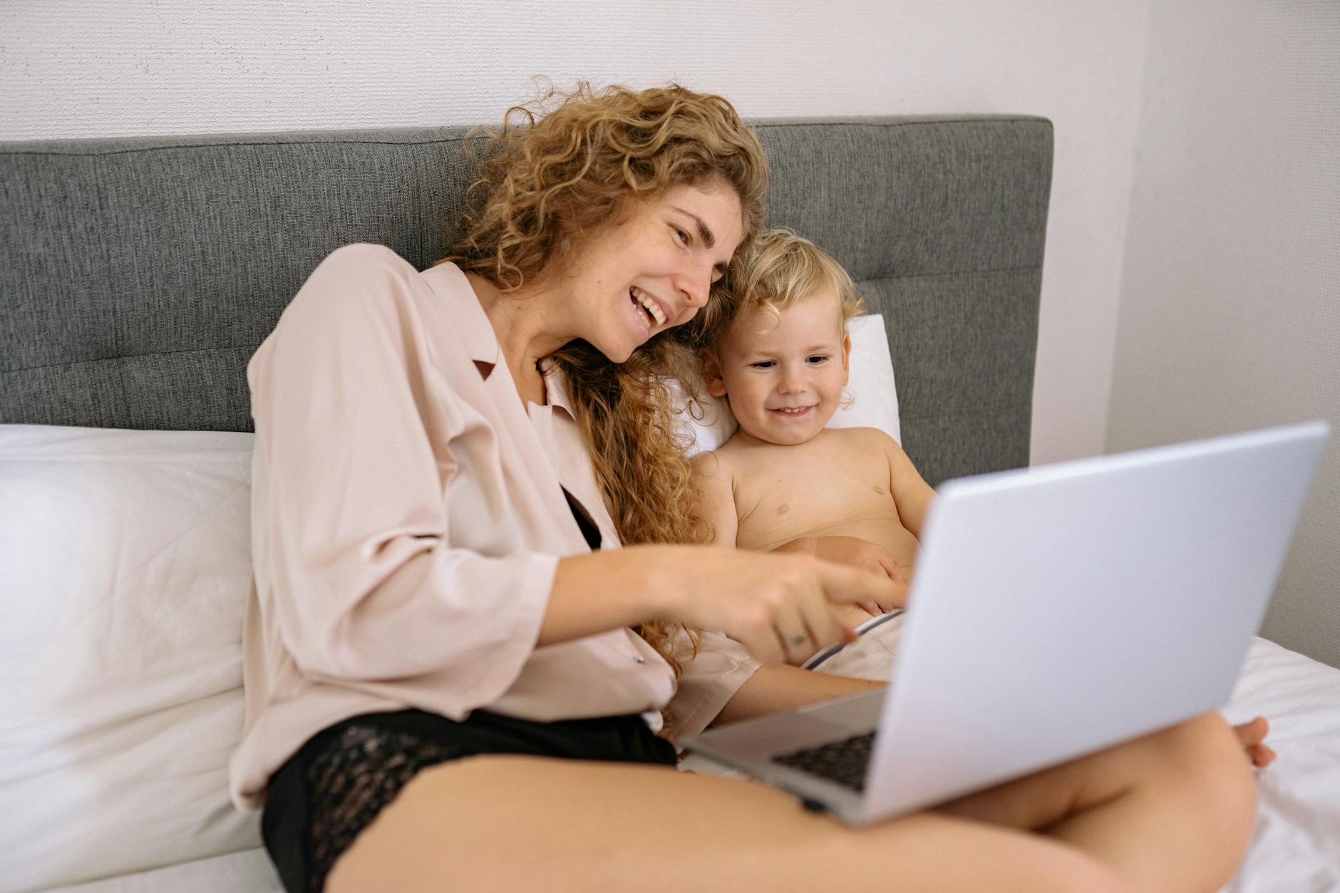 A mother and child enjoying digital time together on a bed, sharing smiles.