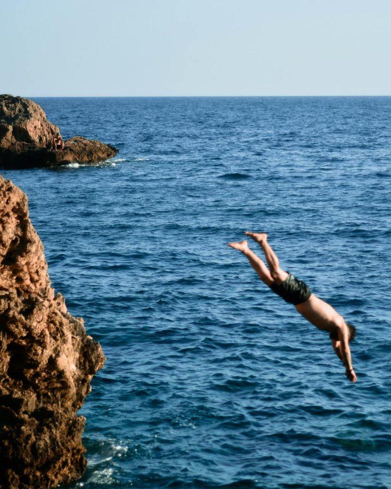 A person diving off a cliff into the Mediterranean Sea in Antalya, Türkiye, captures a stunning summer adventure scene.