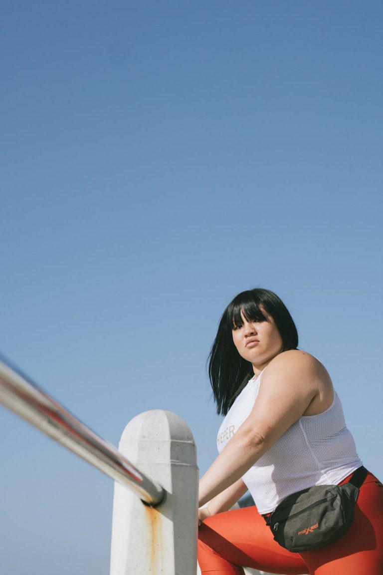 A confident plus size woman in workout attire poses against a clear blue sky.