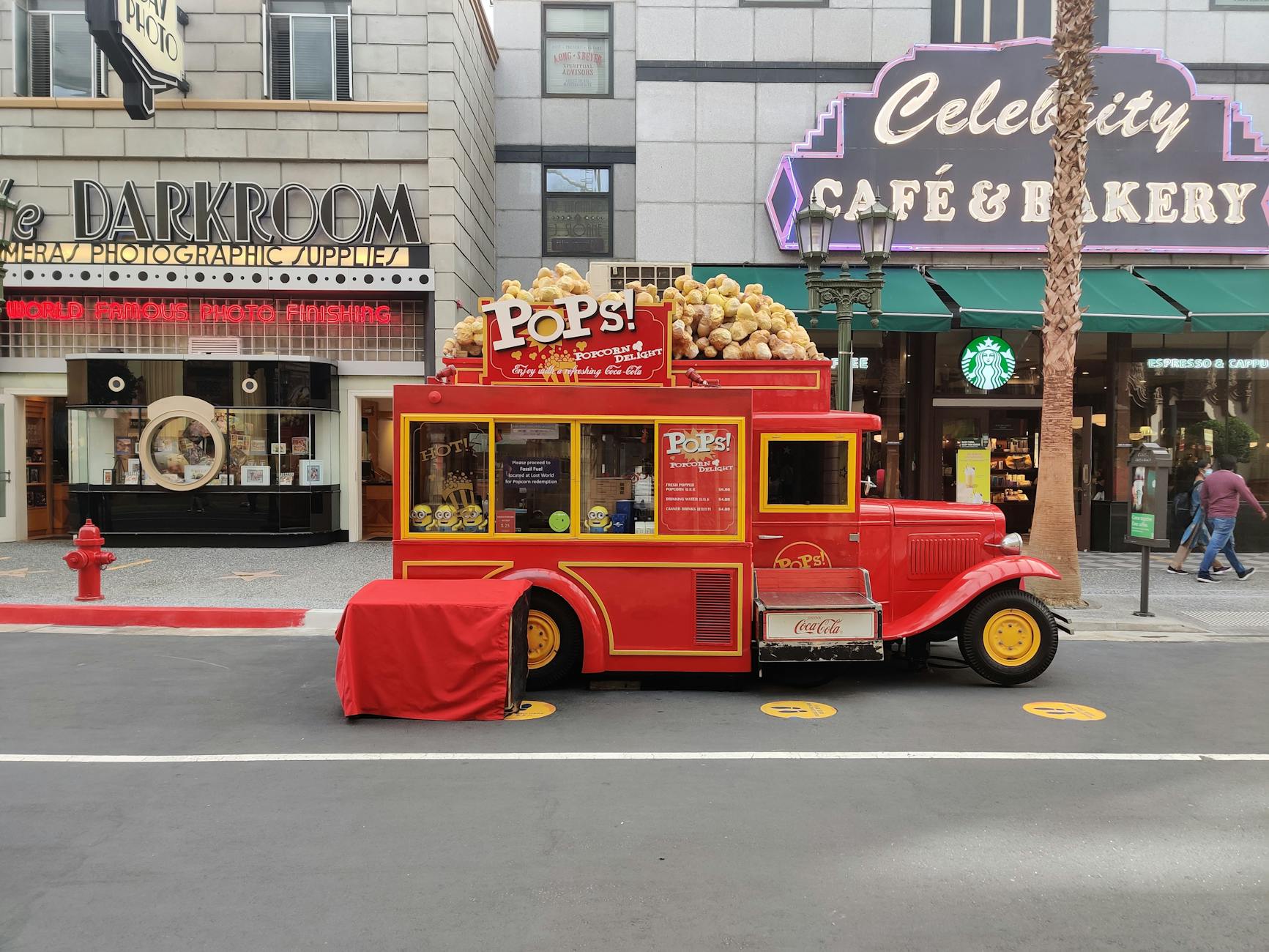 Colorful vintage popcorn truck outside cafes and shops on a bustling street.