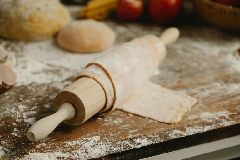 Wooden rolling pin with soft thin dough on table with spilled flour in kitchen