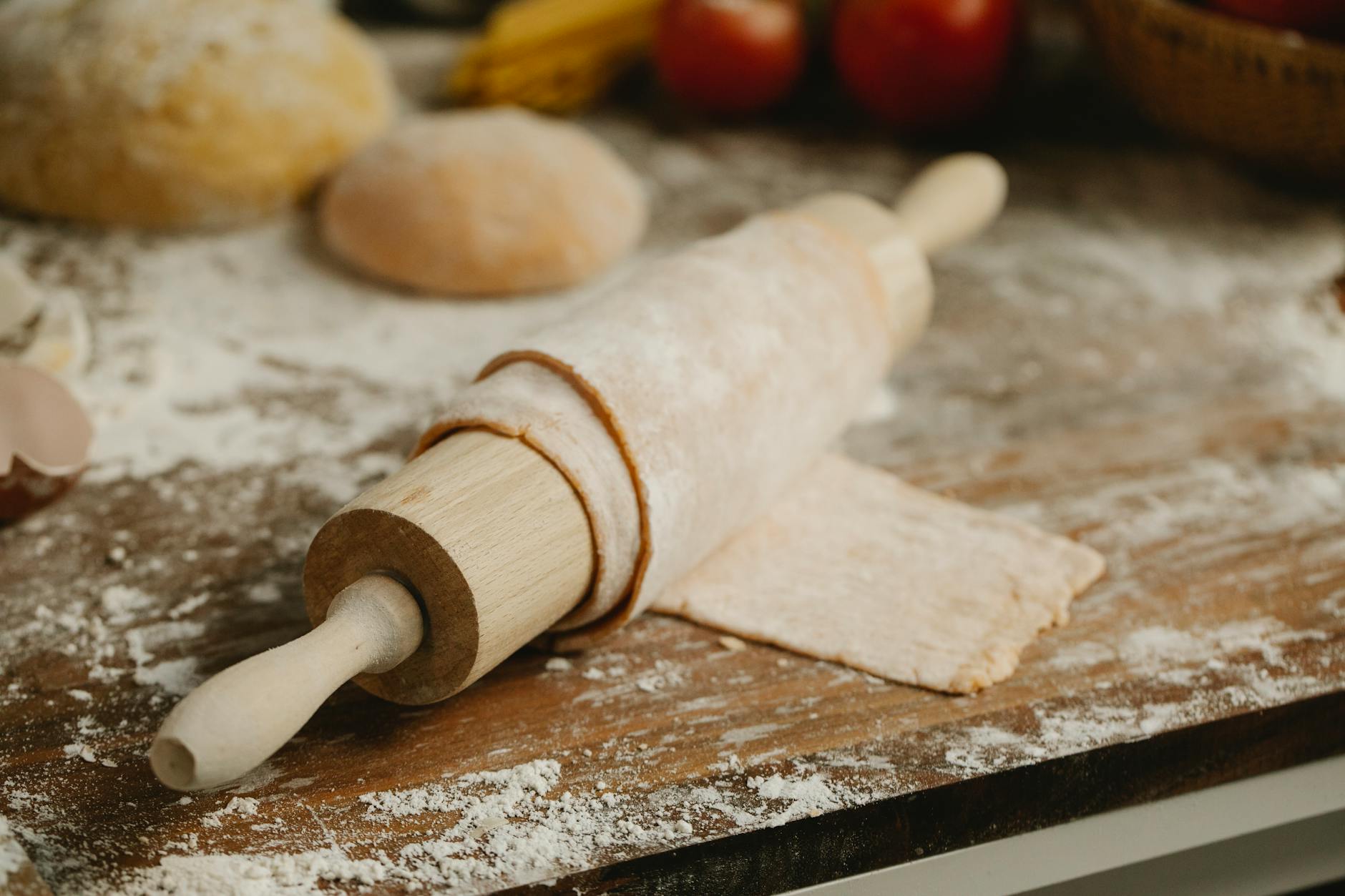 Wooden rolling pin with soft thin dough on table with spilled flour in kitchen