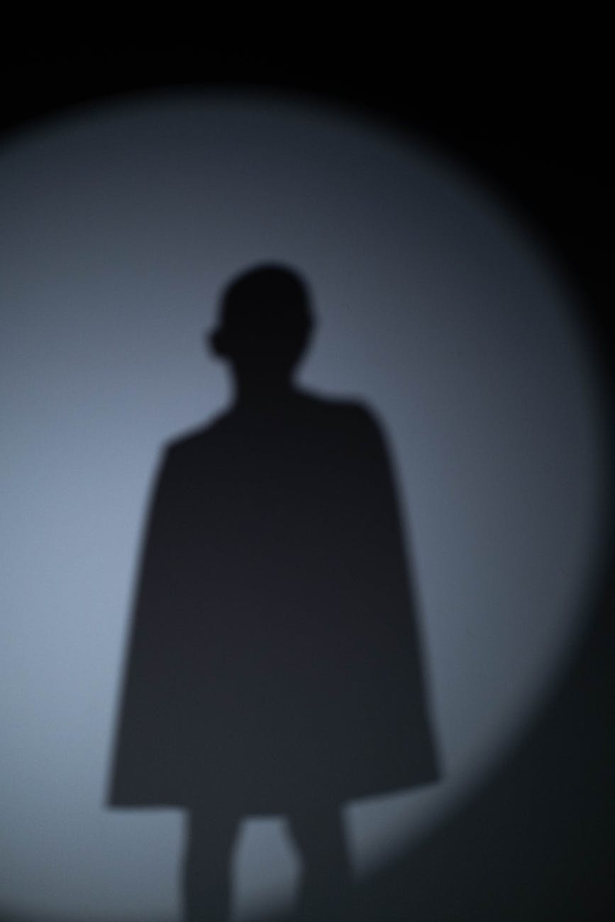 Blurry silhouette of a superhero pose against a spotlight on a gray background.
