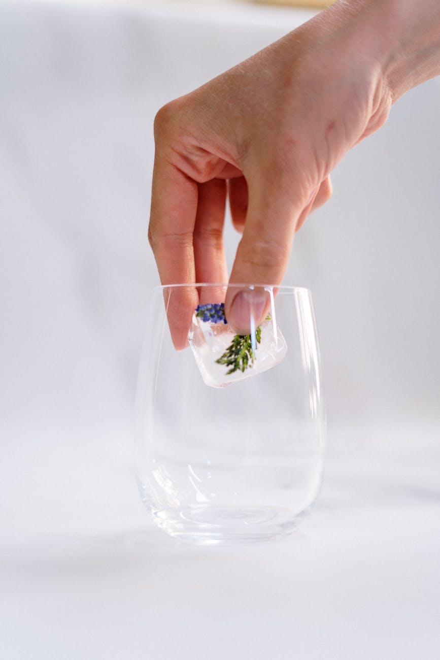 A hand places a floral ice cube in an empty glass, ready for a refreshing drink.