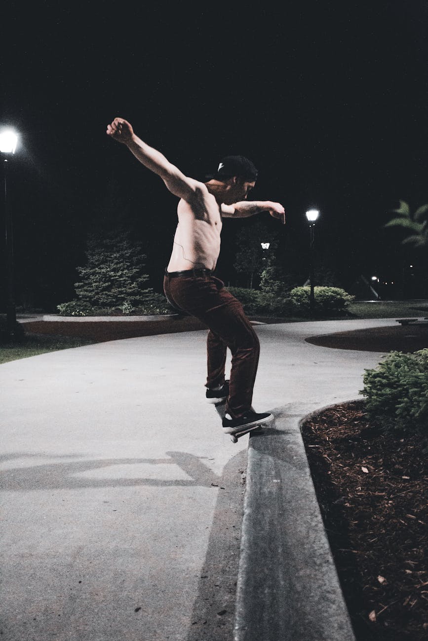 Young man performing a skateboarding trick in a park at night, showcasing athleticism and urban lifestyle.