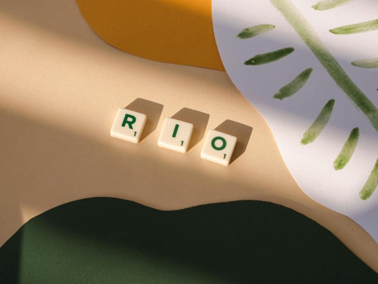 Artistic arrangement of Scrabble tiles spelling 'Rio' among abstract paper cutouts, with vibrant colors and shadows.