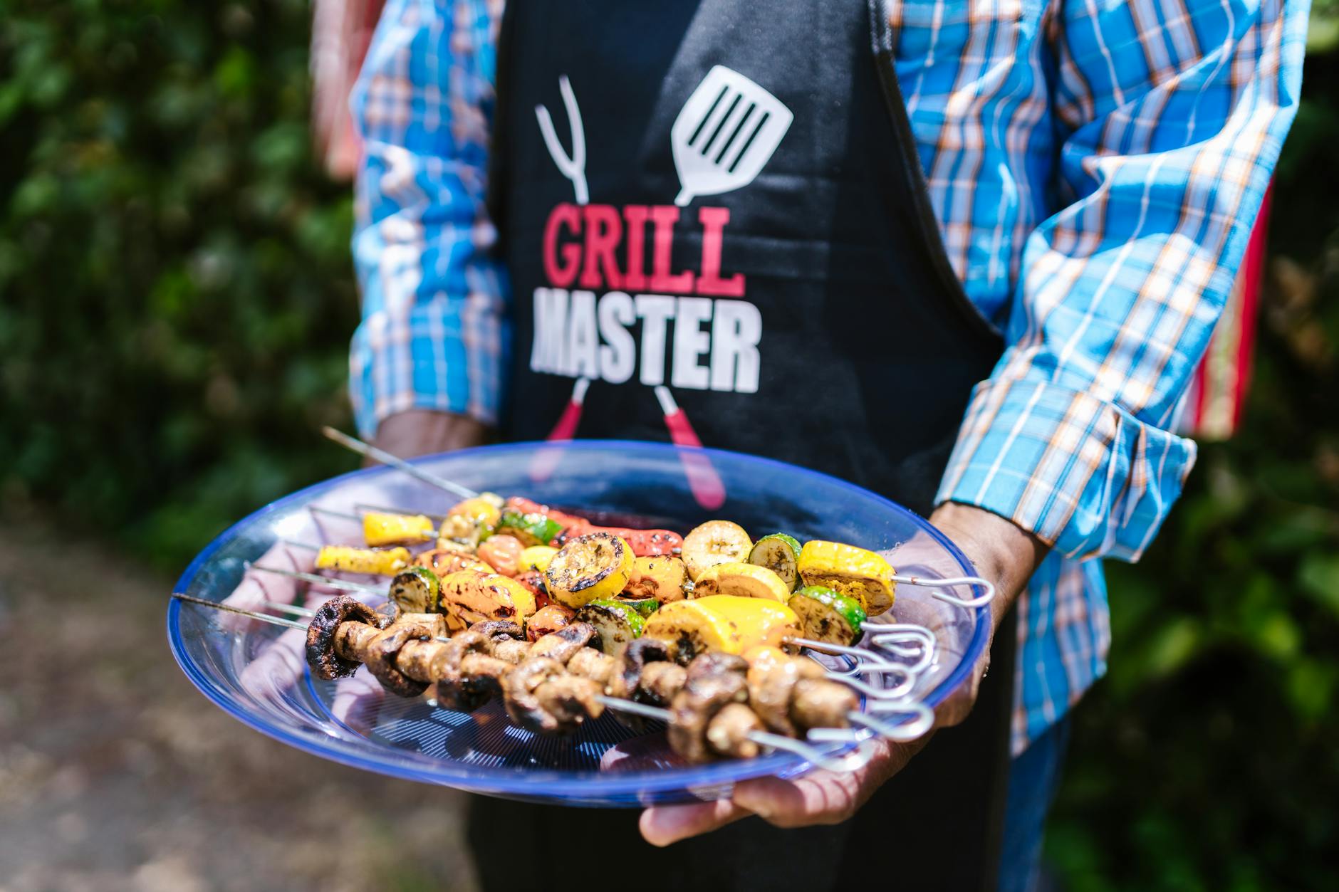 A Grill Master holding a plate of colorful grilled vegetable skewers outdoors.