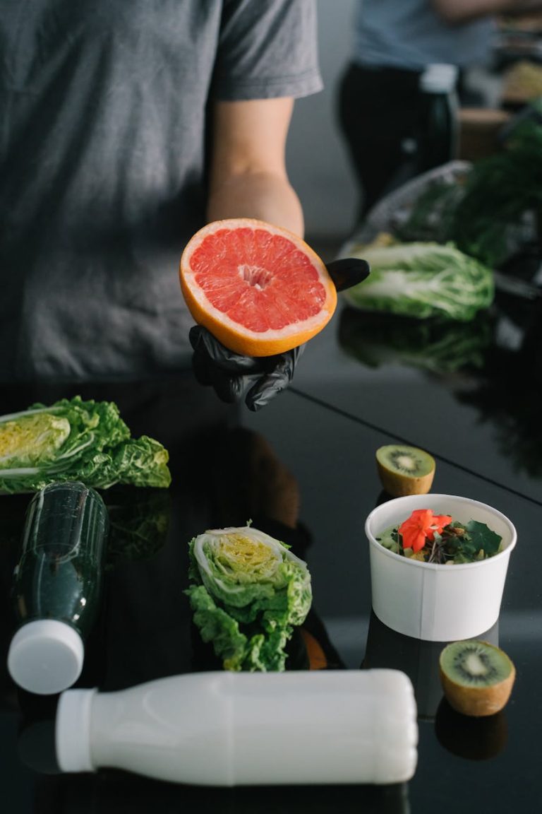 Person preparing a healthy meal with fresh grapefruit, kiwi, and lettuce.