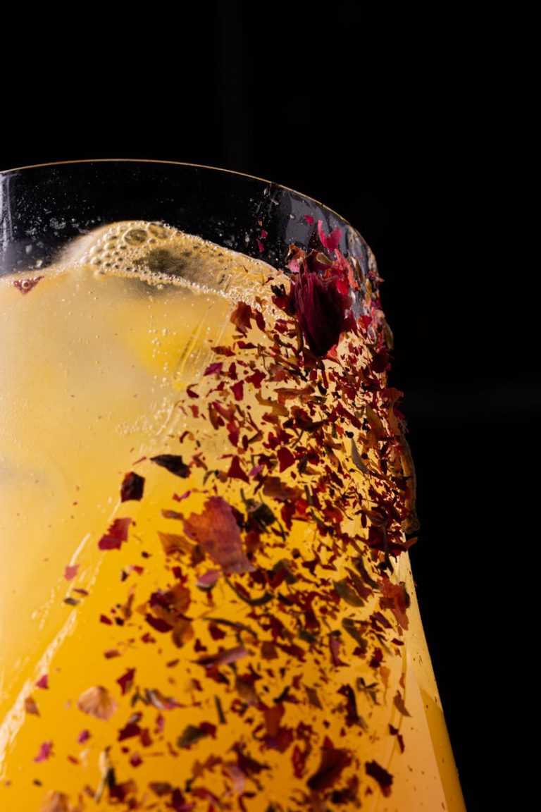 Refreshing floral-infused iced drink with vibrant petals against a dark background.