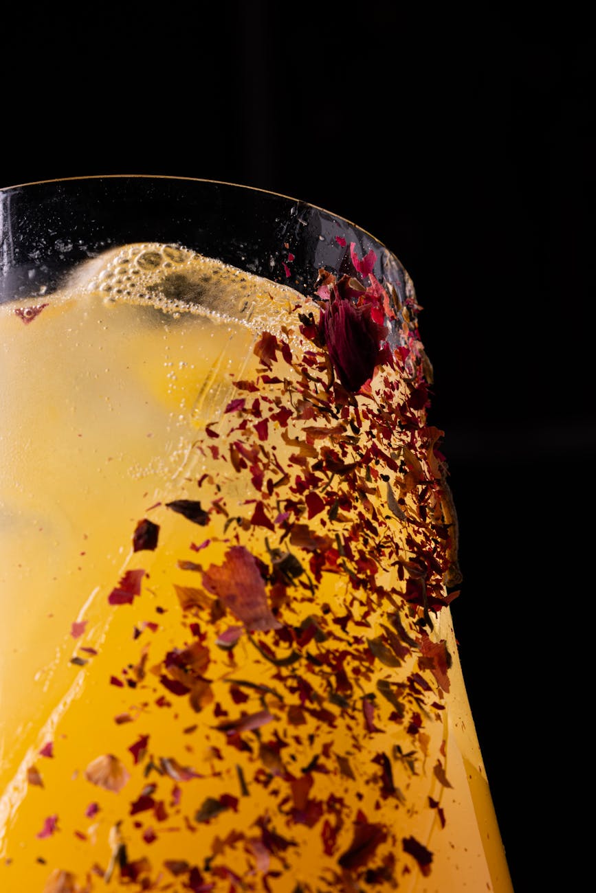 Refreshing floral-infused iced drink with vibrant petals against a dark background.