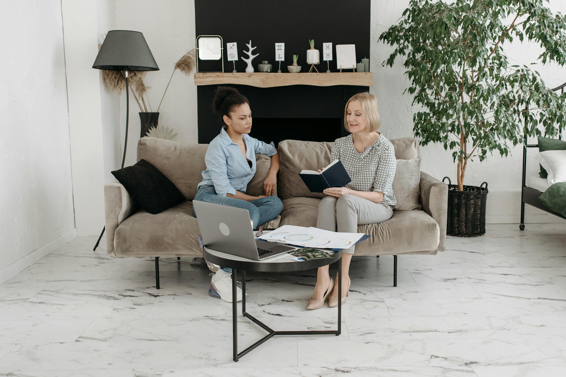 Two women having a professional meeting in a stylish, minimalist living room with laptops and books.