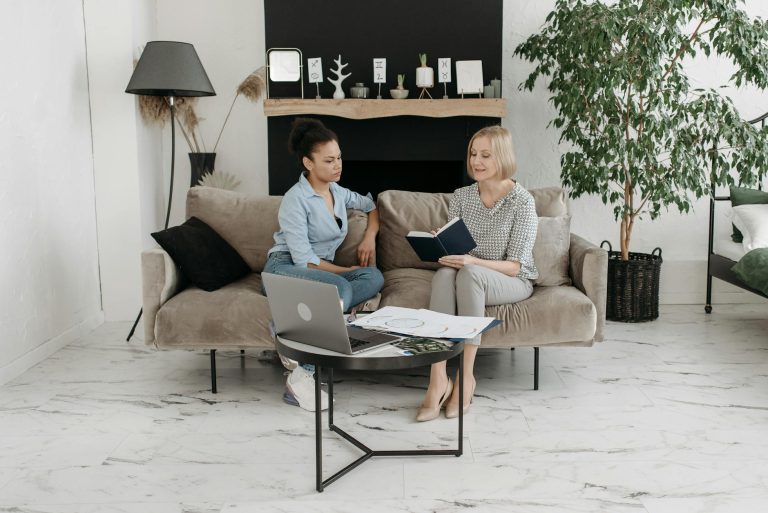 Two women having a professional meeting in a stylish, minimalist living room with laptops and books.