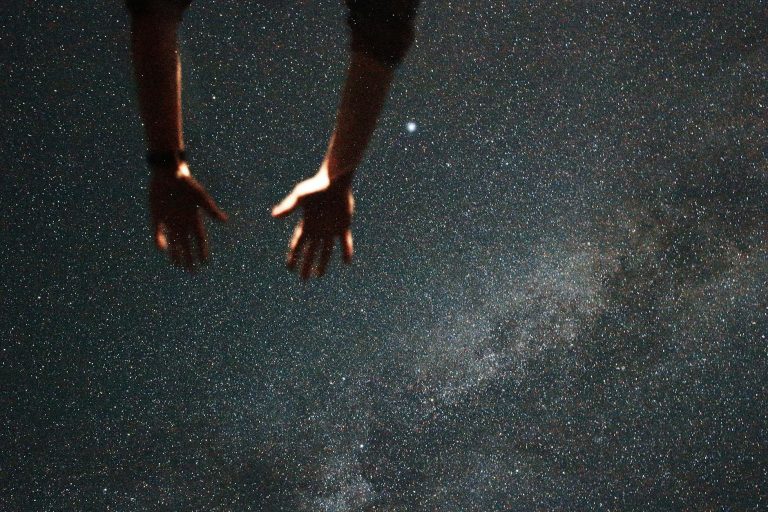 Silhouetted hands reaching towards the starry night sky, capturing a moment of wonder.