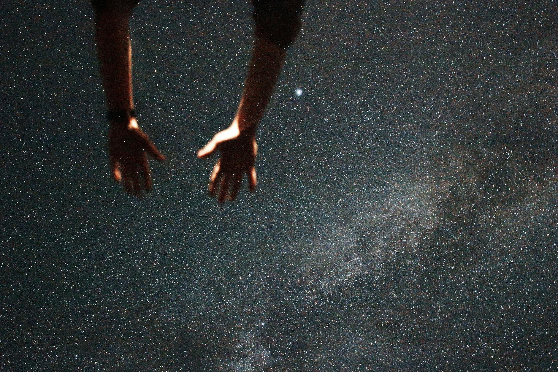 Silhouetted hands reaching towards the starry night sky, capturing a moment of wonder.