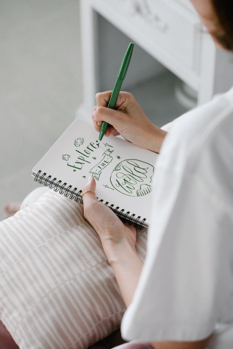 Woman writing creative calligraphy in notebook with green pen, creating inspiring words.