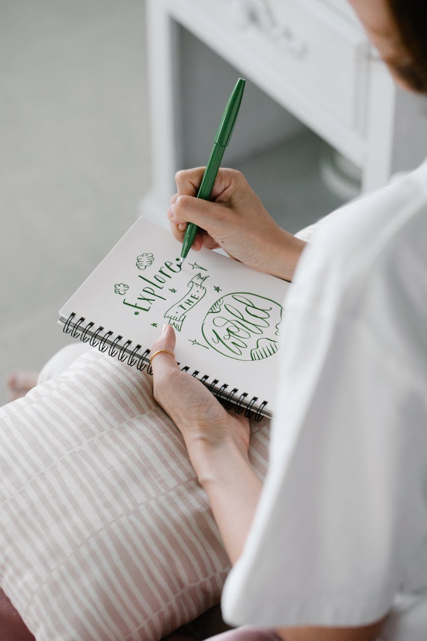 Woman writing creative calligraphy in notebook with green pen, creating inspiring words.