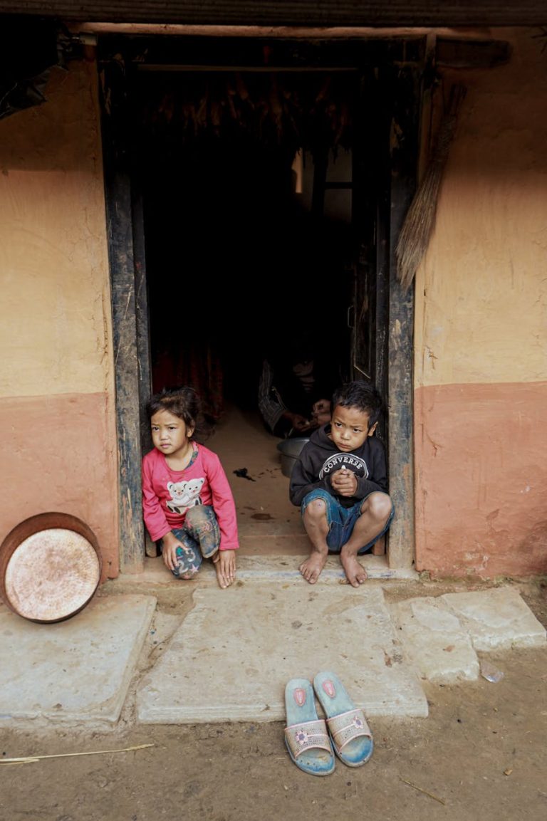 Two children sitting in a rural doorway, capturing innocence and simplicity.
