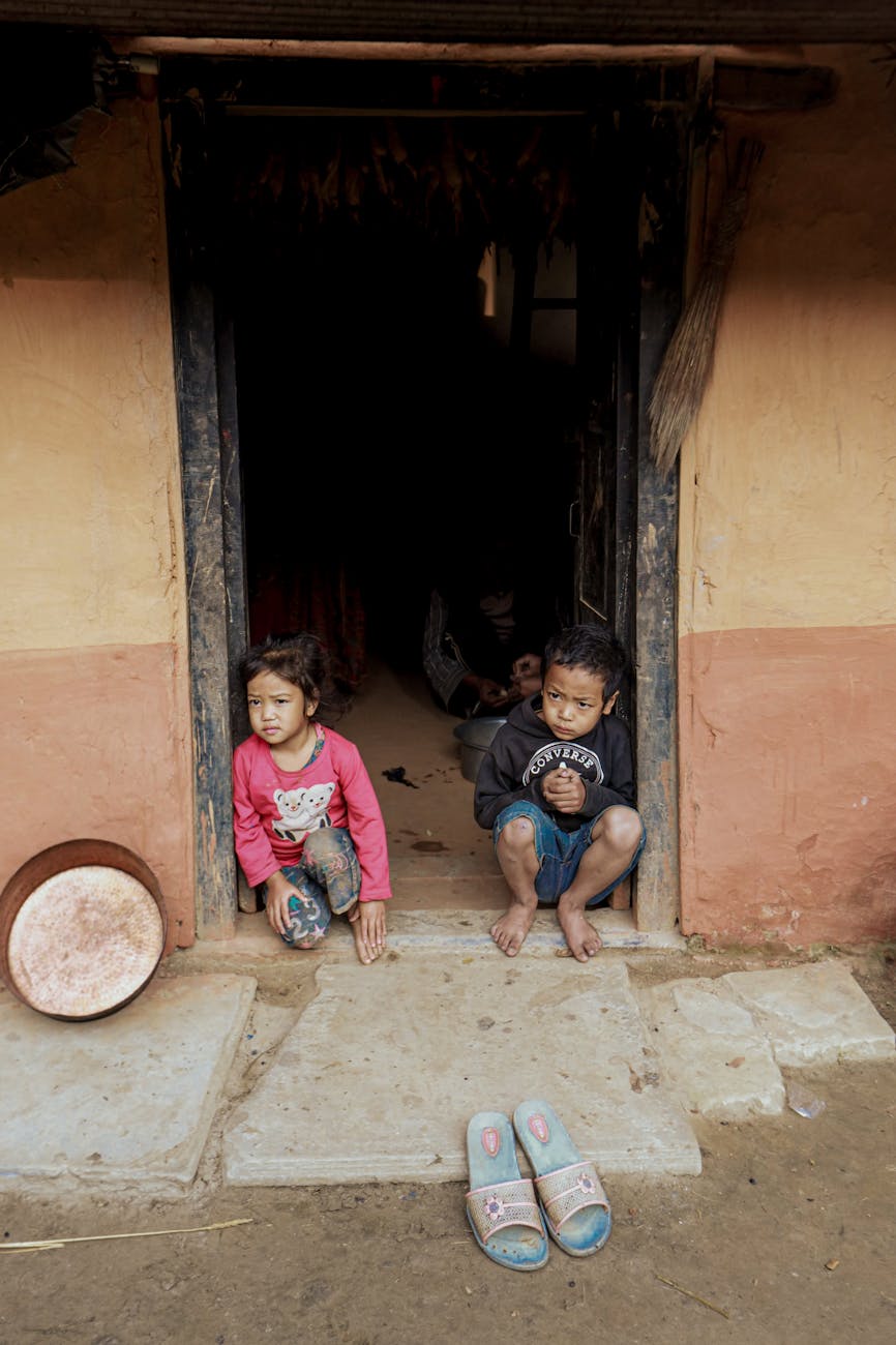 Two children sitting in a rural doorway, capturing innocence and simplicity.