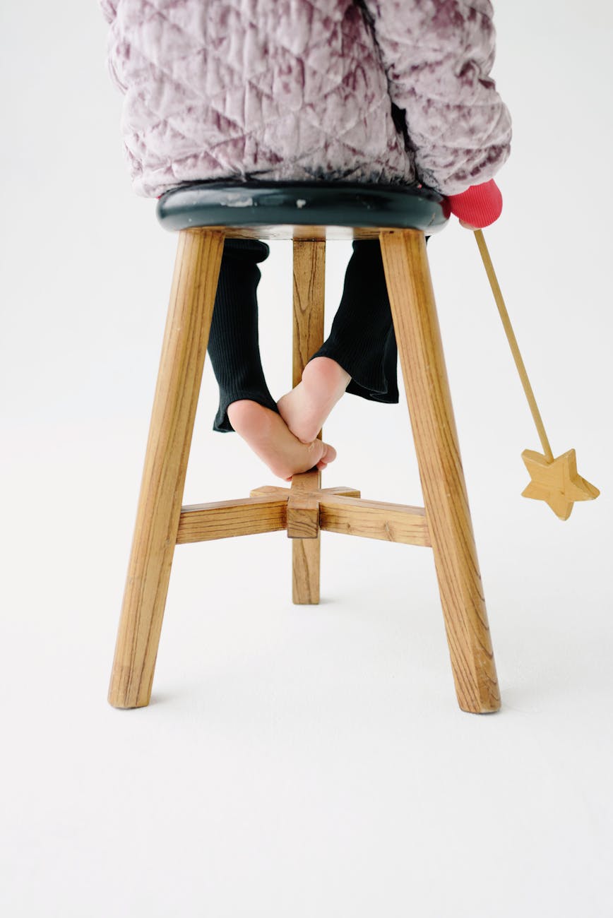 Back view of a child sitting on a stool holding a magic wand.